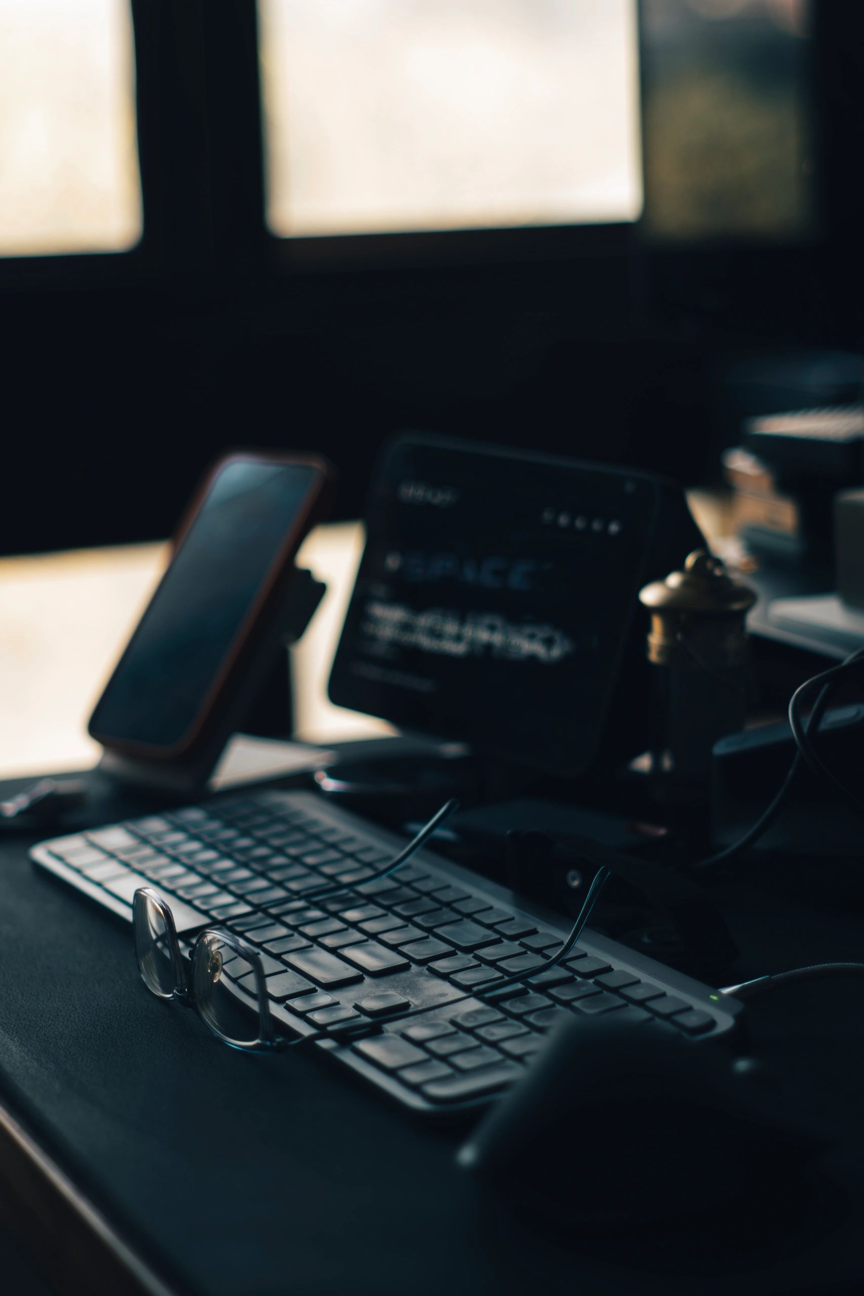 Moody Home Office Desk with Keyboard, Glasses, Smartphone and Tablet in Warm Window Backlight, Remote Work Concept